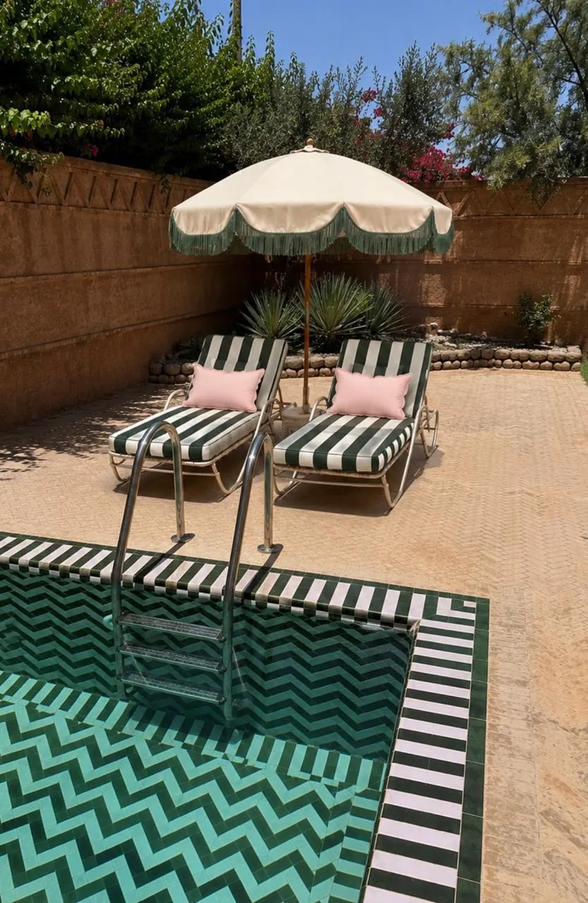 Green striped sun loungers by the pool with fringed umbrella